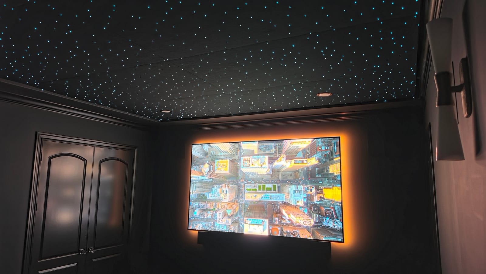 A finished home theater: a fibre-optic star ceiling, a large screen with a warm glow behind it, and wall sconces